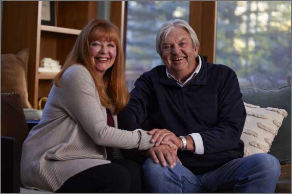 Picture of a smiling man and woman sitting together on a couch holding hands